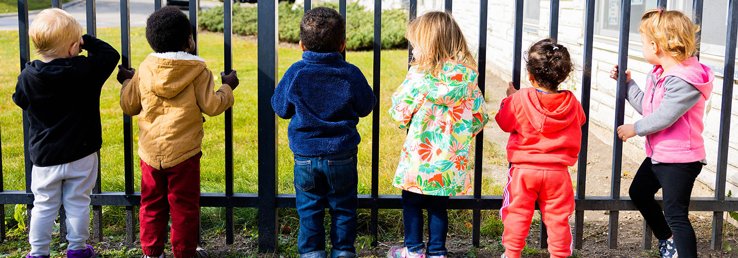 Group of toddlers and small children standing near a fence at Child Development and Family Center