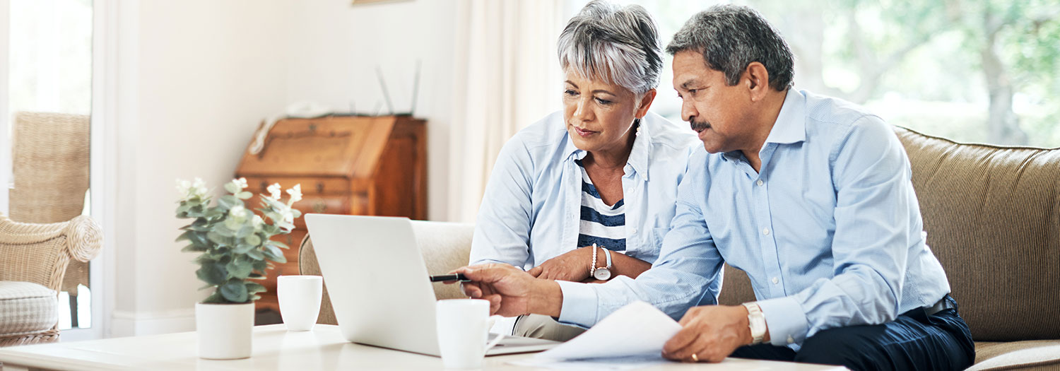 Two people looking together at a laptop. The man is pointing at the screen while holding papers in his hand.