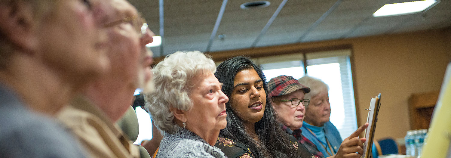 NIU student interacting with a group of elderly people in a meeting room setting